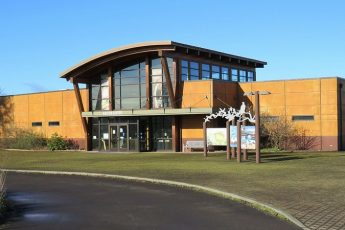 Visitor Center at Tualatin River National Wildlife Refuge. The center is a golden brown building with a glassed entry with a high glass atrium and an arching roof.