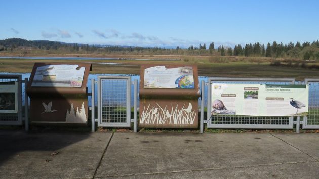 Low fence and informational signage at visitor center observation deck with wetlands in the distance at Tualatin River National Wildlife Refuge.