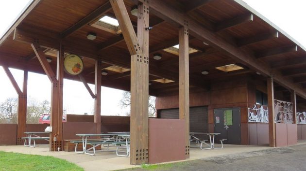 Building with covered open area containing several picnic tables near trailhead.